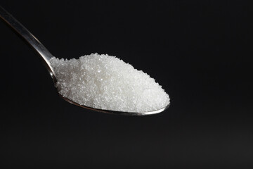 spoon of white sugar on a black background
