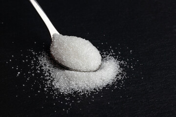 spoon of white sugar on a black background