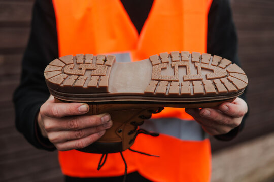 Worker in a reflective safety vest holding a rugged work boot, close-up of the thick non-slip sole, showcasing durable industrial footwear for construction and heavy-duty environments.
