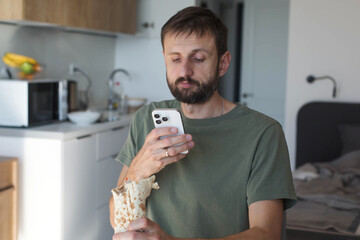 Man in a modern kitchen photographs his shawarma wrap with a smartphone. Casual home environment, relaxed moment, capturing food before eating, everyday lifestyle scene.