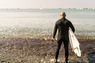 Man in wetsuit holding surfboard looking at ocean