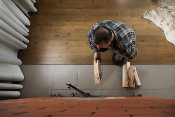 Naklejka premium Caucasian adult man holding wooden log near open stove door while heating bright indoor room with rustic brick construction. Winter Firewood Routine Preparing and Lighting a Wood Stove