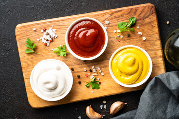 Ketchup, mayonnaise and mustard in the bowls on black background.