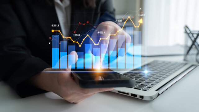 A business professional reviews financial trends on a smartphone while using a laptop. Digital graphs illustrate data, aiding in informed decision-making and strategy development. Scalp