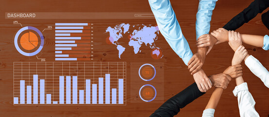 A high-angle view of diverse hands joining together on a wooden table with colorful dashboards and...