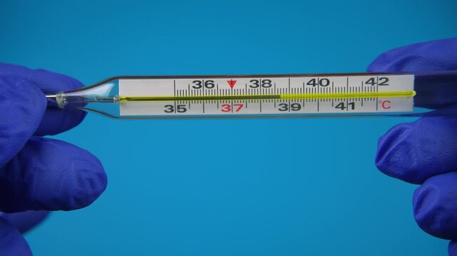 Doctor holding medical mercury thermometer. High body temperature on blue background.