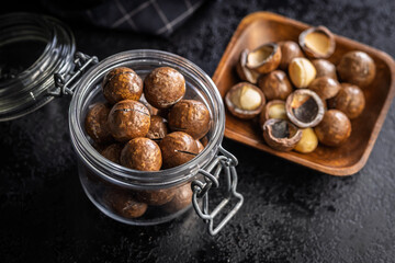 Tasty macadamia nuts in jar on black table.