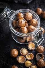 Tasty macadamia nuts in jar on black table.