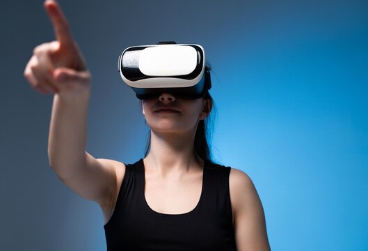 Woman interacting with virtual interface using VR headset and extended hand in clean futuristic blue studio