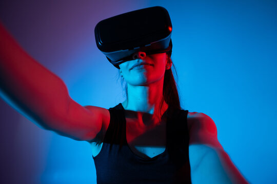Woman exploring immersive virtual reality experience with VR headset in vibrant blue and red studio lighting