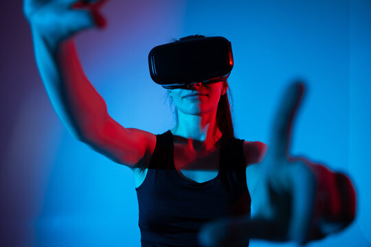 Woman wearing VR headset reaching toward virtual elements in bright neon studio environment and vivid light