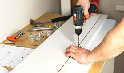 The process of assembling white cabinet furniture using a screwdriver