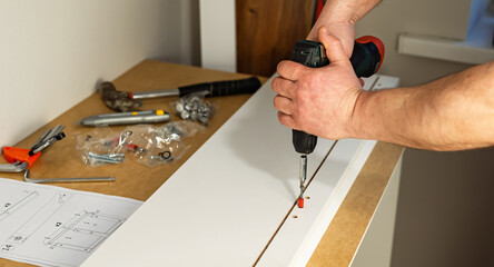 The process of assembling white cabinet furniture using a screwdriver