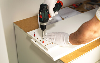 The process of assembling white cabinet furniture using a screwdriver