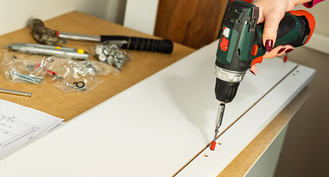 The process of assembling white cabinet furniture using a screwdriver