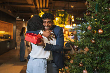 Happy diverse couple exchanging christmas gift at office party