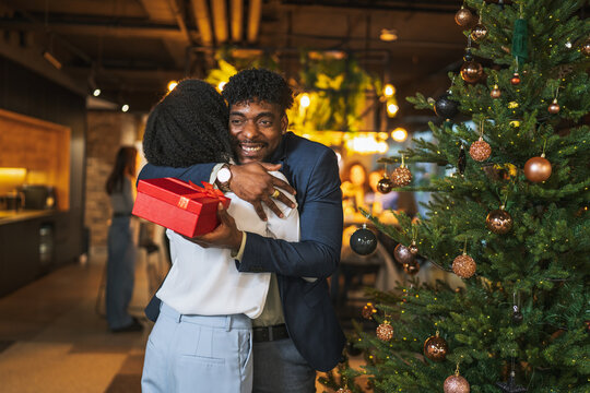 Happy diverse couple exchanging christmas gift at office party