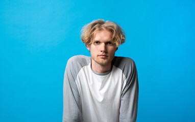 Thoughtful young man leaning slightly forward with serious expression on bright blue background