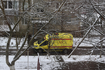 An ambulance near a multi-story reinforced concrete panel building. Winter in a Russian city. Typical residential development in Russia.