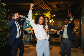 Diverse colleagues dancing and singing karaoke at office christmas party