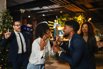 Diverse colleagues celebrating and singing karaoke at office christmas party