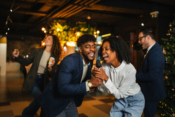 Diverse office colleagues singing karaoke at christmas party