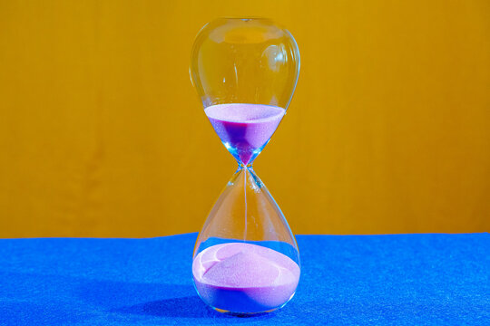 Hourglass in operation with pink sand falling and piling up at the base.