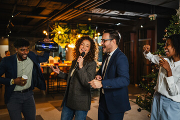 Fototapeta premium Diverse colleagues singing karaoke at office christmas party