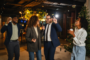 Diverse colleagues singing karaoke at office christmas party