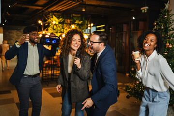Diverse colleagues singing karaoke at office christmas party