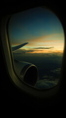Naklejka premium A jet engine and wing are seen through an airplane window during a colorful sunset over the clouds.