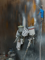 A spray gun hangs from a wall, covered in paint splatters, with paint buckets nearby. Concept of creative process, artistic work or industrial maintenance.