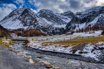 Davos Sertig. Alpine Stream Beneath Snow Capped Peaks, Meadow Dusted With Fresh Snow, Golden Larch Trees Along Rocky Creek Bank, Overcast Sky Casting Soft Light, Clear. High quality photo