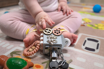 Toddler hands hold a vintage mechanical lock with chains and gears against a colorful rug. Concept of curiosity, exploration, and learning through play and discovery.