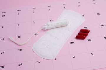 Menstrual products and pain relief on pink calendar tracker. Cycle management. 