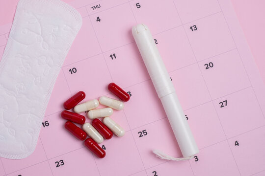 Menstrual products and pain relief on pink calendar tracker. Cycle management. 