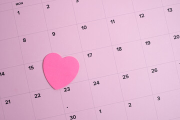 Pink heart sticker on a monthly calendar. Romantic date planning. 