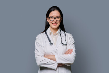 Portrait of smiling female doctor in white lab coat with stethoscope on gray background