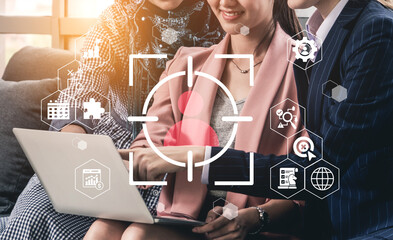 Three businesswomen collaborate over a laptop in a modern office, showcasing a target graphic and digital elements, reflecting teamwork and innovation. Gantry
