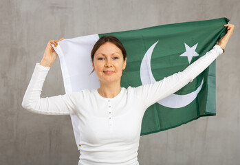 Smiling relaxed woman in casual wear waving national flag of Pakistan while looking at camera at...