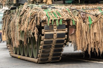 Close-up view of a military tracked tank covered in camouflage netting, showing its heavy armored treads and weathered fabric strips