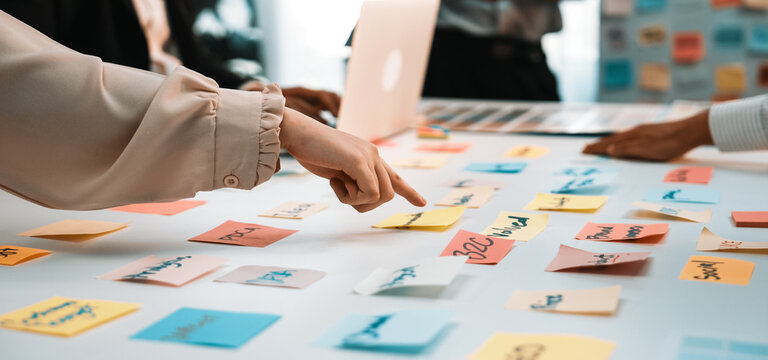 A diverse group of professionals engages in a vibrant brainstorming session, surrounded by colorful sticky notes on a table, showcasing teamwork and idea generation. SACTR - Powered by Adobe