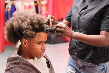 Afro stylist grooming young man's curly hair from right side in salon