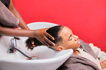 Afro man having his hair rinsed at salon sink from side view by stylist