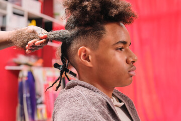 Afro young man getting braids with top hair loose and bottom braided from side view