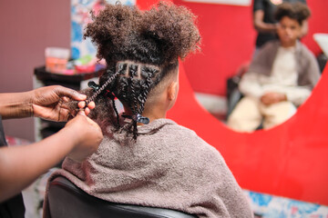 Afro man getting braids from behind with blurred reflection in salon mirror