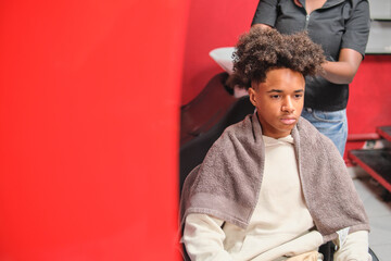 Afro man seated in salon chair reflected in mirror with red wall beside