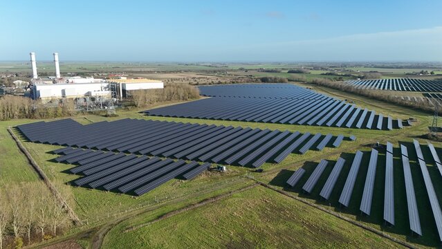 Aerial view of solar panels arrayed in geometric precision against the backdrop of a power plant under a vast sky, Centenary Way, Spalding, England, United Kingdom.