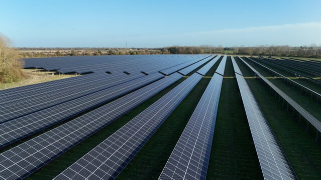 Aerial view of rows of solar panels stretching into the horizon, reflecting the clear sky above the green fields, Centenary Way, Spalding, England, United Kingdom.