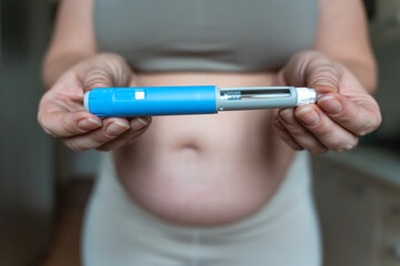 GLP-1 injection pen held by woman in front of abdomen, weight management concept